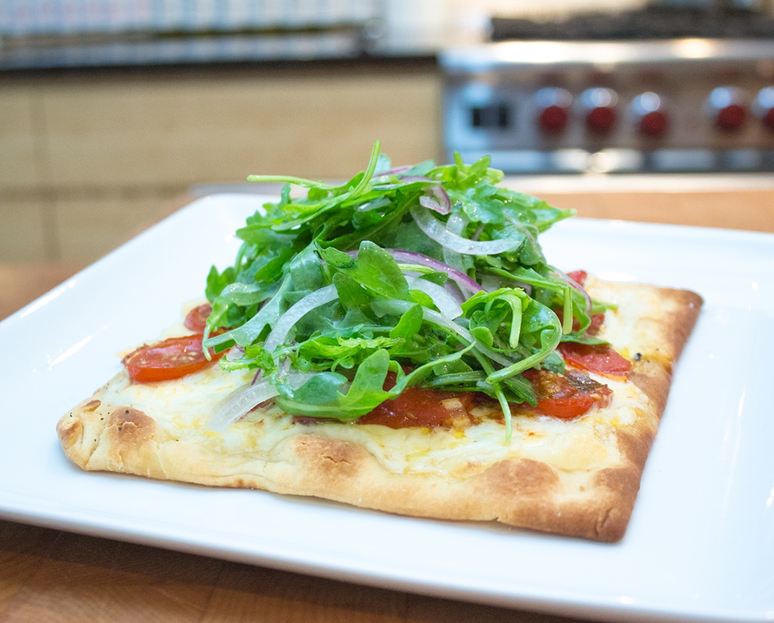 Slow roasted cherry tomato pizza with mozzarella topped with arugula salad